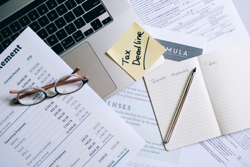 A photo showing a bank statement, notebooks for income and expenses, and a post it stuck to a laptop that says "tax dealine!".